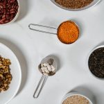 Flat lay of assorted grains, seeds, and nuts in bowls and cups on a white surface.
